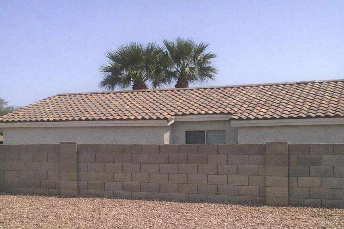 The barrel tile roofline of a Phoenix stucco house with fan palms behind it under a clear sky