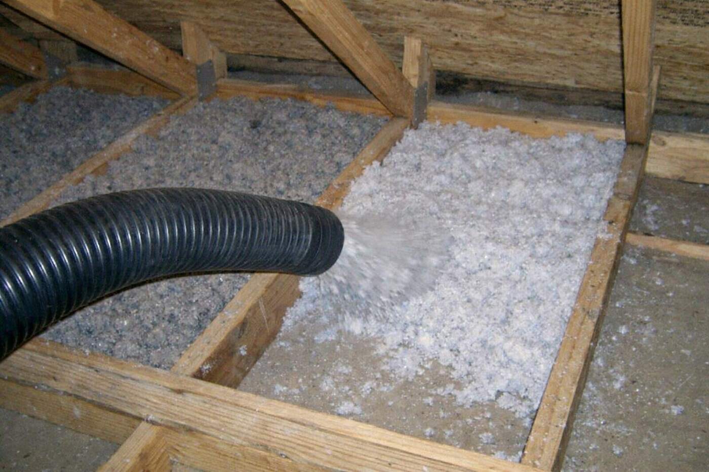 An insulation hose filling a joist bay with fresh loose fill in an attic