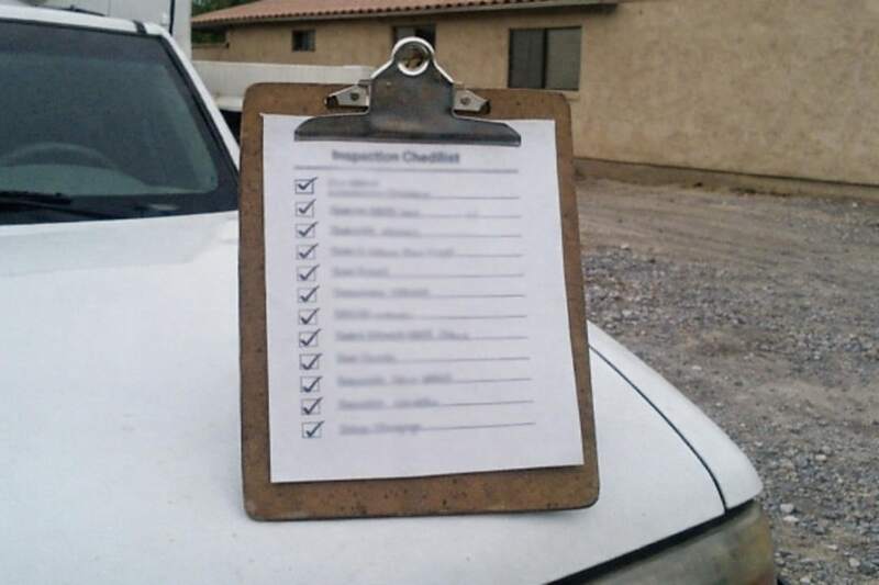 An inspection checklist on a clipboard resting on the hood of a work truck in a gravel driveway