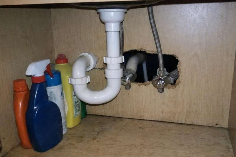 The cabinet under a kitchen sink, with supply pipes passing through an unsealed hole in the back panel