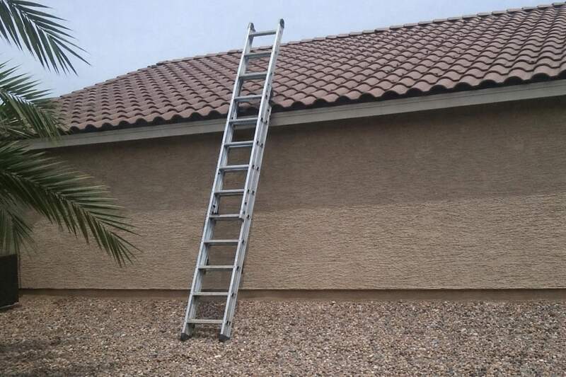 An extension ladder standing against the eave of a concrete barrel tile roof on a stucco house