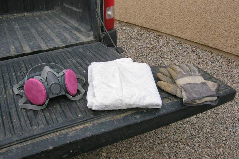A half-face respirator, a folded protective coverall and gloves laid out on a truck tailgate